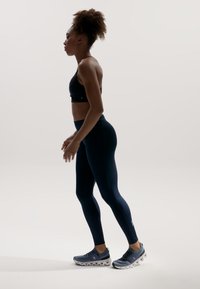 Schwarzer Sport-BH, marineblaue Leggings und graue Laufschuhe. Fokus auf Passform und Bewegung, die sportliches Design und Gewebestruktur zur Schau stellen.