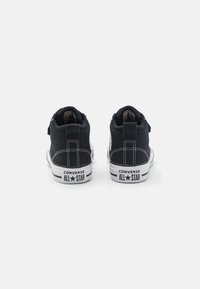 Tênis de cano alto em lona preta com sola de borracha branca. Inclui costura branca contrastante e o logótipo "Converse All Star" no calcanhar.
