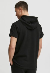 Sort kortærmet hoodie lavet af tekstureret materiale. Har en rullet kant og justerbar hætte. Enkel, minimalistisk design.