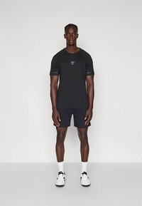 Must musta lühikeste varrukatega spordisärk, millel on väike logo, kombineeritud mustade lühikeste pükste, valgete tossude ja valgete sokkidega.