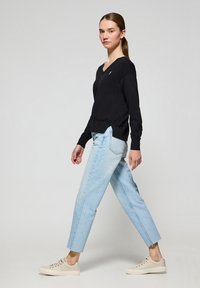 Svart v-ringad tröja med ribbade ärmar, ljusblå högmidjade jeans och beige sneakers med snörning. Modell i sidoprofil.