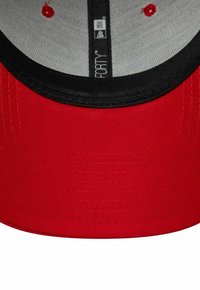 Rote Kappe mit schwarzem Schirm, aus strukturiertem Stoff gefertigt. Das Innere ist mit einem grauen Futter und roten Lüftungslöchern ausgestattet. Markenlabel sichtbar.