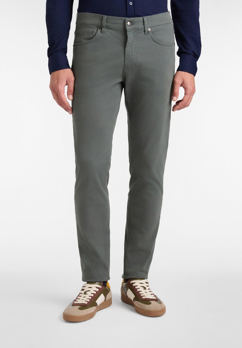 Sive bombažne hlače s slim fit krojem, petimi žepi in kontrastnim šivanjem, v kombinaciji z večbarvnimi nizkimi športnimi copati.