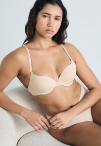 Hautfarbener, geformter BH mit verstellbaren Trägern und glatter Textur; dazu passender hoher Slip in der gleichen Farbe, beide zeichnen sich durch ein minimalistisches Design aus.