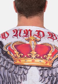 Kurzarmhemd mit einem Kronen-Design in Rot- und Goldtönen, verziert mit Strasssteinen und ergänzt durch Flügelillustrationen.