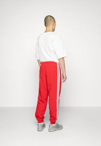 Joggers rojos ajustados con rayas laterales blancas, cinturilla elástica y puños. Combinados con una camiseta blanca de corte holgado y zapatillas grises.
