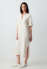 Beige linnen jurk met een V-hals, korte mouwen, zijsplitten en een comfortabele pasvorm, gecombineerd met witte sneakers. Glad textuur en lichtgewicht.