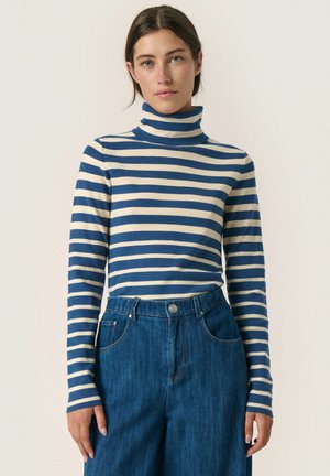 Zilā un krēmkrāsas svītraina turtlenecks, ribota tekstūra, garas piedurknes, apvienots ar džinsēm ar platiem kājiem, kas aprīkoti ar priekšējiem kabatām un pogu aizdari.