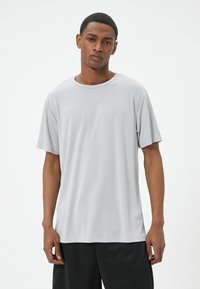 Camiseta de manga corta gris claro hecha de tejido transpirable, con cuello redondo y corte relajado, combinada con pantalones cortos deportivos negros.