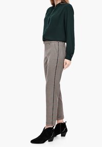 Mörkgrön blus med långa ärmar, kombinerad med rutiga byxor med sidopaneler och svarta ankelbooties med texturerad yta.