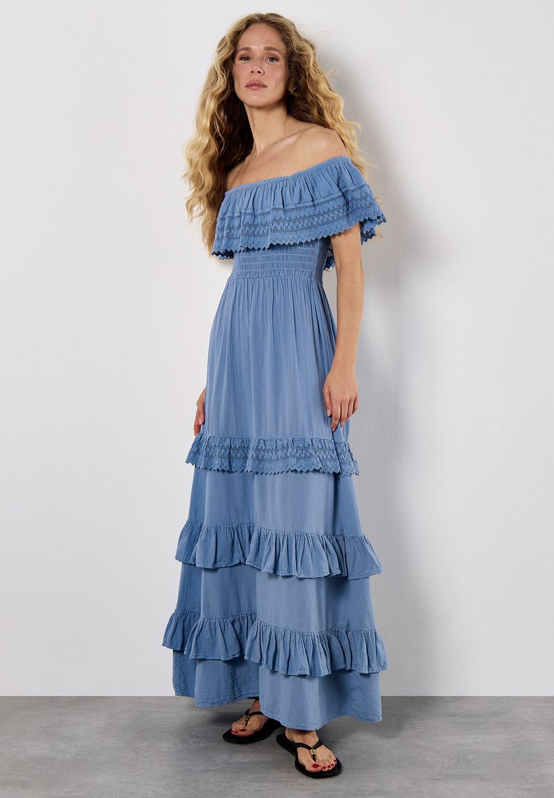 Helles blaues, schulterfreies Maxikleid mit Rüschenschichten, Spitzenbesatz und tailliertem Oberteil. Der Stoff wirkt weich und fließend.