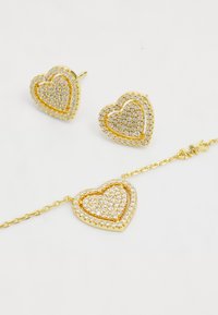 Guld hjerteformede øreringe og armbånd, prydet med klare rhinsten. Struktureret overflade, kædessa på armbåndet, og skinnende finish.