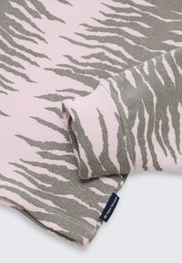 Primo piano di un tessuto a strisce tigre rosa e grigio con una manica piegata e una piccola etichetta blu scuro con la scritta "Tom Tailor."