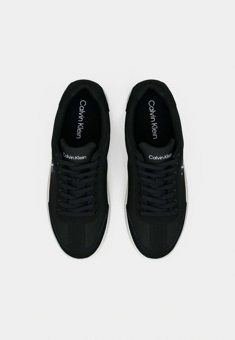Black athletic shoes with a fabric upper, lace-up design, white rubber sole, and "Calvin Klein" logo on the tongue and side.