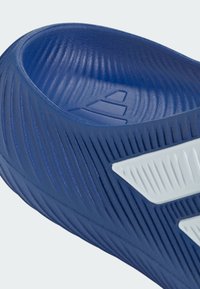 Primer plano de sandalia azul sin cierre con superficie texturizada y diseño angular blanco en el lateral, destacando los contornos ergonómicos de la plantilla.