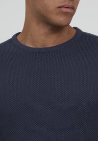 Pulover tricotat navy cu o suprafață texturată, guler rotund și guler cu nervuri. Materialul pare moale și puțin gros. Design minimalist.