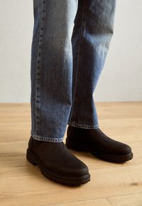 Bottines noires avec une texture lisse, bout rond et semelle en caoutchouc. Associées à un jean bleu slim avec un léger décoloration.