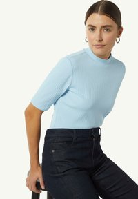 Jasnoniebieska prążkowana bluzka z krótkim rękawem i wysokim kołnierzem, zestawiona z ciemnymi dżinsami. Materiał ma gładką teksturę i dopasowany krój.