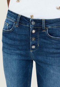 Jeans in denim blu scuro con vita alta, chiusura a cinque bottoni e dettagli decorativi con pietre sugli abbottonamenti. Texture sottile e design classico.