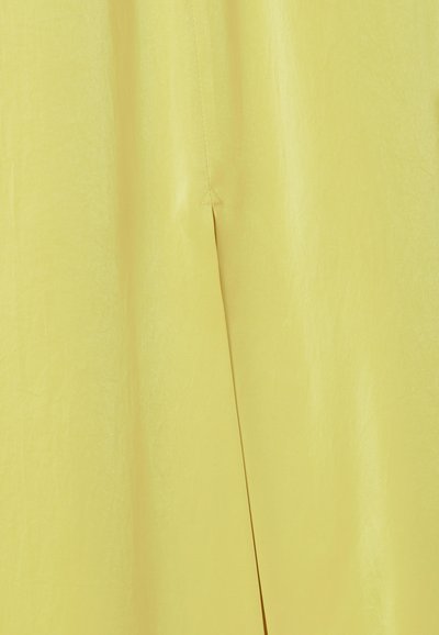 Tessuto giallo con una piega verticale e un dettaglio di cucitura triangolare vicino al centro superiore.