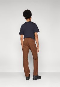 Brown cargo pants with multiple side pockets, made of durable fabric. Paired with a short-sleeve navy t-shirt and black shoes.