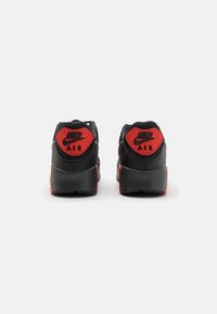 Sneaker nere con accenti rossi, caratterizzate da un rivestimento posteriore testurizzato, un collare imbottito e una visibile ammortizzazione Air nella suola.