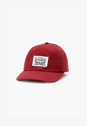 Red cotton baseball cap with adjustable strap, featuring a rectangular white patch with black text and graphic designs on the front.