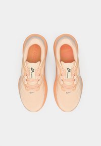 Een paar perzikkleurige Nike hardloopschoenen met veters en "Run Structure" labels, van bovenaf bekeken op een witte achtergrond.