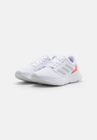 Zapatillas de running blancas de Adidas con rayas gris claro y acentos en naranja en el talón, exhibidas una al lado de la otra sobre un fondo blanco.