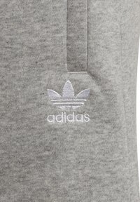 Grå textilväv med en slät yta; har en tonalt broderad Adidas-logotyp och klassisk tre-stripes-design i vitt.