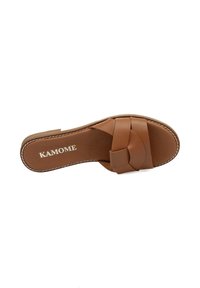 Sandal de color marrón, tipo slip-on, con una amplia correa anudada, parte superior de cuero suave y una plantilla acolchada. Nombre de la marca "KAMOME" impreso en la plantilla.