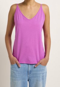 Rosa ärmlös topp med V-halsdesign, tillverkad av mjukt tyg. Har tunna axelband och en avslappnad passform, i kombination med ljusblå jeans.