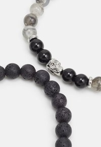 To perlearmbånd med sort lava sten, sorte og grå perler, samt en sølvkraniumaccent på det ene armbånd.