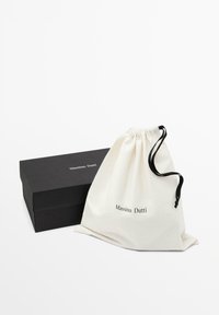 Borsa a tracolla in tela color crema con cordino nero, con il logo "Massimo Dutti". Accompagnata da una scatola rettangolare nera.