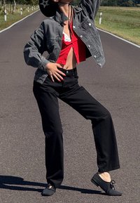 Chaqueta de mezclilla gris, top corto rojo, pantalones negros de pierna ancha y zapatos negros con cordones. De pie en una carretera con un fondo de césped.