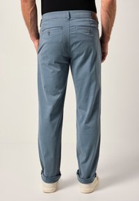 Ljust blå byxor med en avslappnad passform, som har två bakfickor med knäppning, uppvikta fållar och en brun läderdetalj vid midjan.