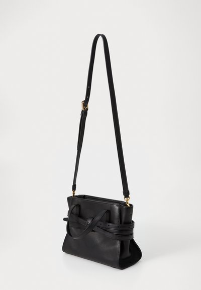 Sac à main en cuir noir avec une forme structurée, une fine bande réglable et un détail de nœud à l'avant. Texture lisse avec des accents en matériel doré.