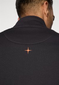 Dark black polo shirt featuring a high collar and a geometric orange star logo on the upper back, made from smooth fabric.