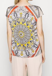 T-shirt à manches courtes présentant un design de mandala coloré et complexe avec des accents jaunes, noirs et rouges sur un tissu léger.