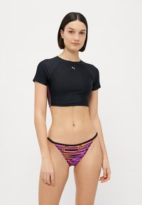 Μαύρο αθλητικό τοπ με κοντά μανίκια και λογότυπο Puma, συνδυασμένο με μασχαλωτό μπικίνι σε πολύχρωμο σχέδιο με αφηρημένα ροζ και μωβ μοτίβα.