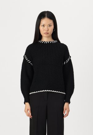 Pull en maille noir avec des accents blancs au col et à l'ourlet, présentant une texture côtelée et des manches à coupe ample.