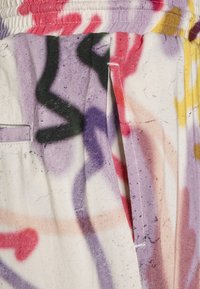 Nahaufnahme von bunter, graffitiartiger Druckstoff mit schwarzen, roten, lila, gelben und rosa abstrakten Formen sowie sichtbaren Nähdetails.