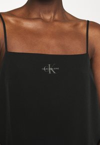 Schwarzes Satin-Camisole mit dünnen Spaghetti-Trägern. Verfügt über einen quadratischen Ausschnitt und ein kleines "CK"-Logo auf der Vorderseite.