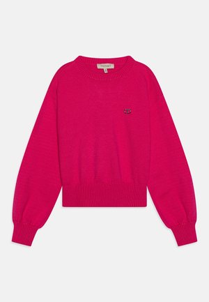 Pull court fuchsia en tissu tricoté doux, avec poignets et ourlet côtelés, arborant un petit logo sur la poitrine.