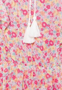 Floral dress in lightweight, textured fabric. Features pink, yellow, and blue floral patterns; accented with white tassels and ruffled trim.