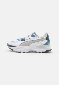 Chaussure de sport blanche et bleu clair avec des panneaux en maille, des accents texturés et une semelle épaisse. Présente des lacets et un col rembourré pour le confort.
