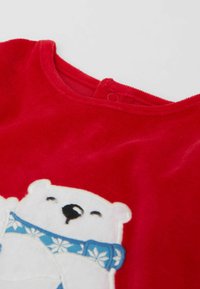 Chemise en velours rouge à manches longues avec un col rond, mettant en avant un ours polaire brodé portant une écharpe bleue et des accents de flocons de neige blancs.