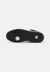 Black skate shoe sole with textured rubber, circular white logo detail, and patterned grip design for traction.