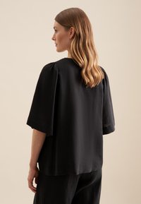 Blusa nera in lino con maniche corte a sbuffo, scollatura arrotondata e vestibilità rilassata. Texture morbida e design minimalista.