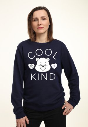 Marineblå sweatshirt med lange ærmer har hvid tekst, der står "COOL TO BE KIND", samt et bjørnegrafik. Blødt stof, afslappet pasform.